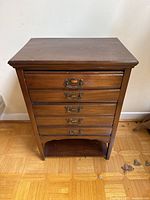 Front view of small wooden chest of drawers showing the five drawers and metal handles.