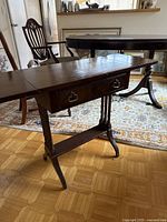 View of the small wooden side table showing expandable leaves and base with drawer and turned legs