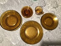 five amber glass pieces: three plates, cup, bowl