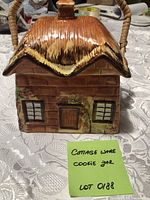 Front view of ceramic cottage cookie jar with thatched roof lid and wicker handle
