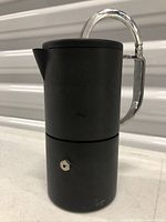 Side view of matte black cylindrical stovetop coffee maker with polished handle
