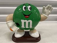 Front view of plastic M&M's Green candy dispenser showing waving hand and logo