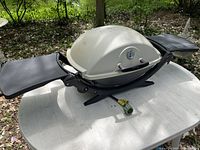 Weber Q 1200 grill with side tables extended on table, hose and regulator visible