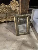 Mirror placed upright on floor showing full gold embossed metal frame and reflection.