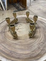 Photo of two golden metal candle holders placed on a large wooden surface, showing their size and detail.
