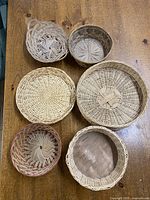 Top-down view of six small woven baskets arranged on a wooden surface, showing varied shapes and weaving patterns.