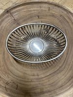 Top and side view of oval silver-tone metal bowl with basket open slats and solid base on a wooden surface.