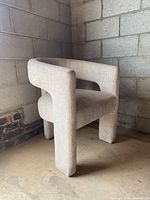 Side view of beige upholstered chair with three legs and curved backrest