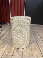 Front view of cylindrical side table showing tiled surface and wooden floor background.