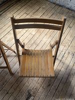 Close-up photo of one wooden folding chair showing slatted wood seat and curved backrest.