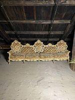 Full view of the ornate vintage couch showing carved wood frame and four distinct backrests, upholstery with floral pattern in gold and beige, long seat cushions, located in a dimly lit space.
