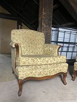 Full side view of vintage floral armchair showing upholstery and wooden curved legs and arm accents.