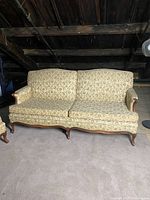 Front view of vintage floral print couch showing fabric pattern, wooden frame, and carved legs in attic storage.