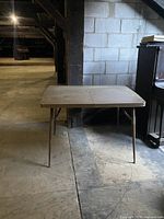 Vintage folding table with wooden top in a warehouse setting, visible rust on metal legs and surface wear on wood.