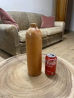 Full view of vintage stoneware gin bottle next to a Coke can for scale, showing tall cylindrical shape and embossed text.