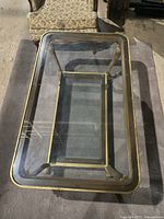 Top view of the vintage glass coffee table showing the ornate gold metal frame and clear glass top with a rug underneath.