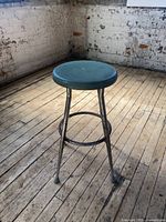 Full view of a vintage steel stool with teal round seat and rusted steel legs placed on a wooden floor.