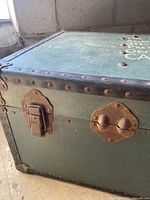 Close-up of the side of the trunk showing a rusted metal latch, corner rivets, and textured green surface.