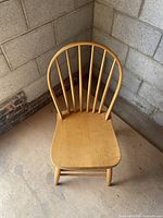 Front view of wooden Windsor style chair with rounded spindle backrest and contoured seat on wooden legs.
