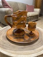 Photo of the pitcher, goblet, and round tray displayed together on a wooden table with a couch in the background.
