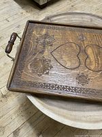 Wooden rectangular serving tray with carved hearts and floral designs, showing corner detail and one wooden handle