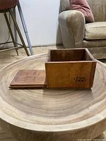Wooden tea box with sliding lid shown fully open on a round wooden table, front branding visible.