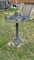 Full view of the green metal bird bath standing on grass with frog figurines around the basin and on the stand.