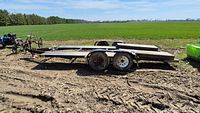 Trailer side view showing dual axle, steel frame and wood deck with ramps