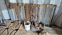 Full view of assortment of heavy-duty chains hanging on wooden rack with accessories and bucket below.