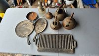 Overview of all items on table showing copper kettles, cast iron pans, grill plate and vintage oil can
