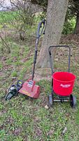 Photo showing Noma Turboshovel 1200 electric shovel, Yardworks electric hedge trimmer, and Earthway wheeled spreader outdoors against a tree on grass.
