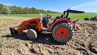 Right-side view of tractor with loader arms and forks installed, muddy tires.