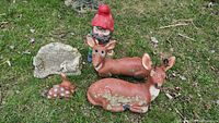 Photo showing various lawn ornaments including a reclining deer, standing deer, a small spotted rabbit, a stone plaque with a rabbit relief, and a garden gnome with a red hat.
