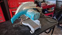 Front-right angle view of the Makita miter saw showing the blue handle, blade housing, and base with wear.