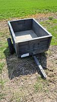 Angle view of Rubbermaid small yardwork trailer showing box interior and hitch tongue on grass.