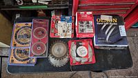 Overview of assorted saw blades and molding set arranged on a black surface, showing various brands and sizes boxed and loose.