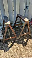 Two custom welded metal saw horses placed outdoors on dirt ground, showing size and condition including rust.