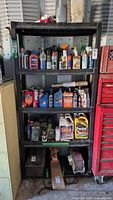 Front view of black plastic shelving unit showing all five shelves and contents for scale. Shelving has signs of wear, located indoors in garage/storage setting.
