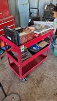 Front and left side view of Torin red metal shop cart with three shelves, visible wear, missing handle, caster wheels fixed to bottom.