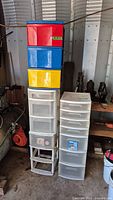 Four plastic storage drawer units stacked and placed side by side in a garage setting with some tools and coiled extension cord visible