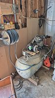 Side view of entire compressor in workshop showing tank, motor and coiled hose
