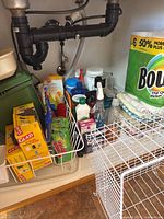 Overview of cleaning supplies, dish rack, and trash bags under sink