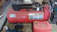 Side view of the red Craftsman air compressor with attached coiled red hose and gasoline tank beside it