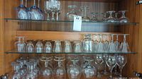Wide shot of multiple glass shelves containing various types of clear glassware including wine glasses and goblets.