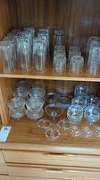 Wide shot of various clear glass drinking glasses and dessert bowls displayed on wooden shelves