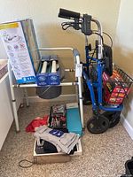 Walker with wheels, equipped with front basket holding boxed items, adjacent to a raised toilet seat and two grab bars on the floor.