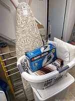 Overall view of ironing board, laundry basket with iron box, and hamper in laundry area
