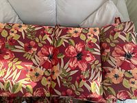 Four patio cushions arranged on seating and floor, showing red fabric with floral pattern of large flowers and green leaves.
