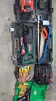 Overview of Black & Decker power tools in cases, two hand saws, battery charger, and air hammer laid out on the ground.