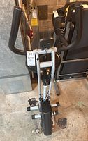 Front view of stationary bike showing handlebars with foam grips, digital monitor, and pedals.